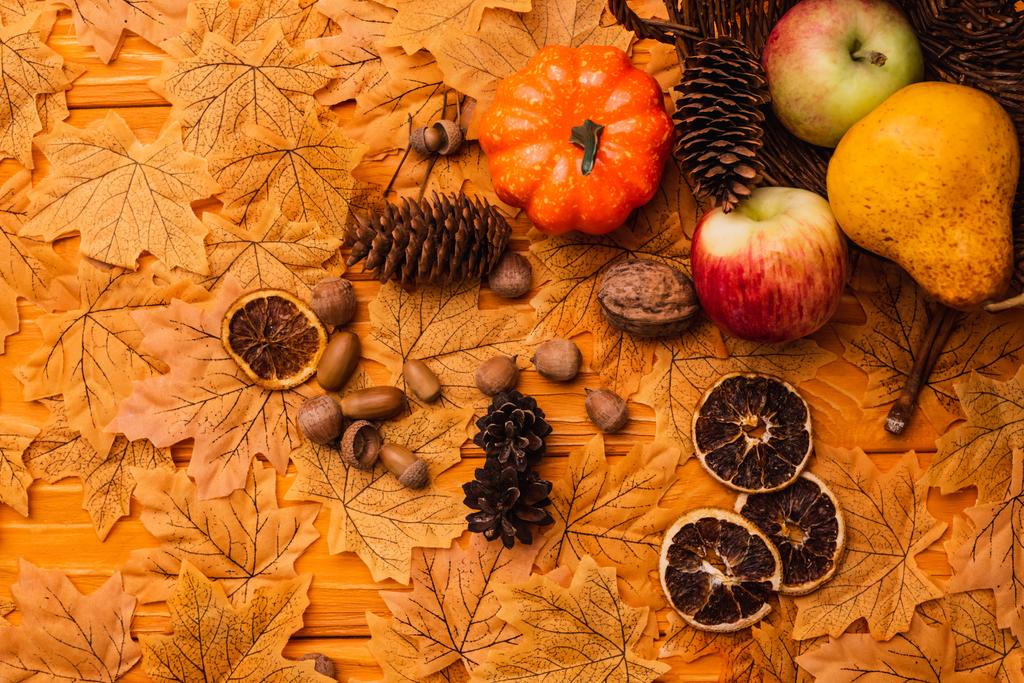 κορυφαία άποψη της φθινοπωρινής διακόσμησης και των τροφίμων διάσπαρτα από ψάθινο καλάθι σε χρυσό φύλλωμα σε ξύλινο φόντο - Φωτογραφία, εικόνα