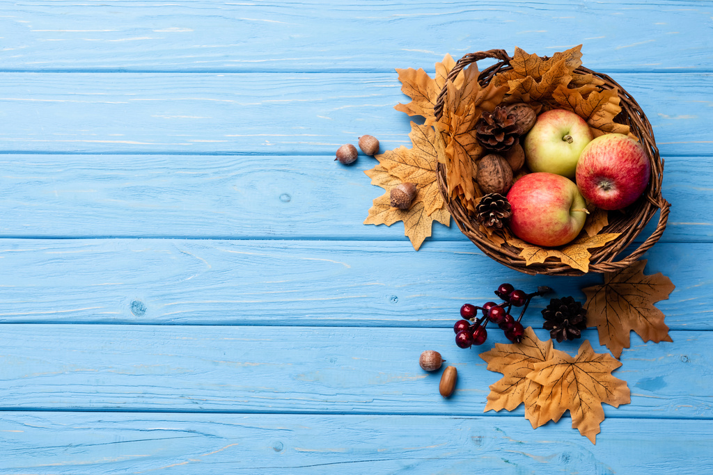 Blick von oben auf herbstlichen Weidenkorb mit Äpfeln, Nüssen und Zapfen auf blauem Holzhintergrund - Foto, Bild