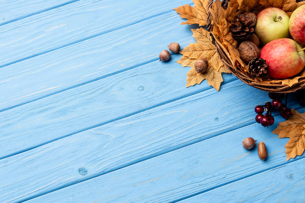 vista superior de la canasta de mimbre otoñal con manzanas, nueces y conos sobre fondo de madera azul - Foto, Imagen