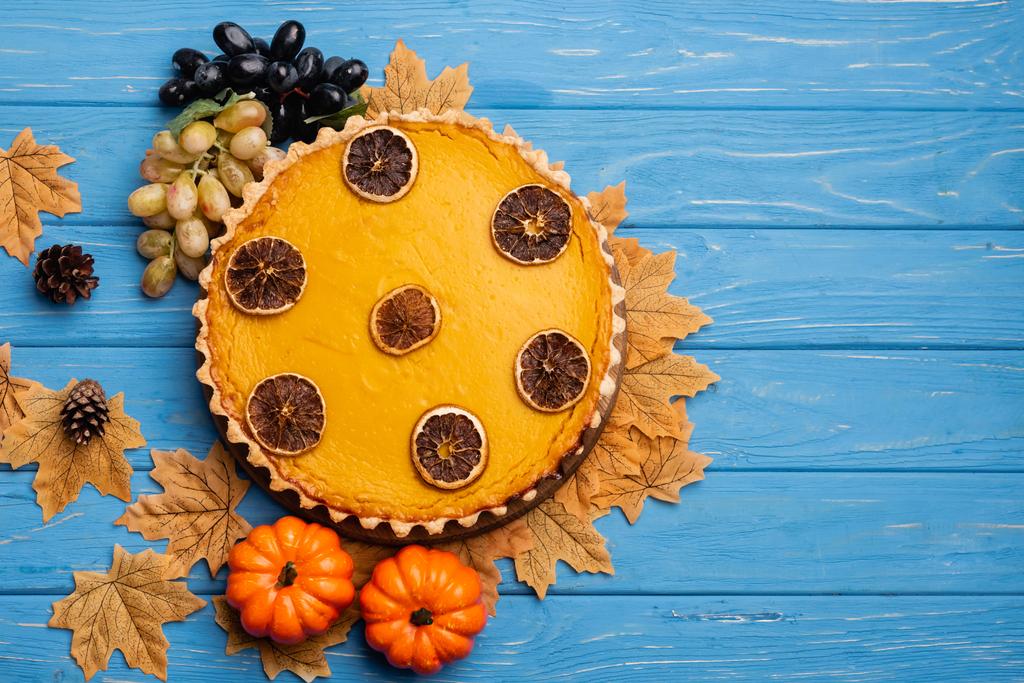 top view of decorated pumpkin pie with golden foliage on blue wooden background - Photo, Image