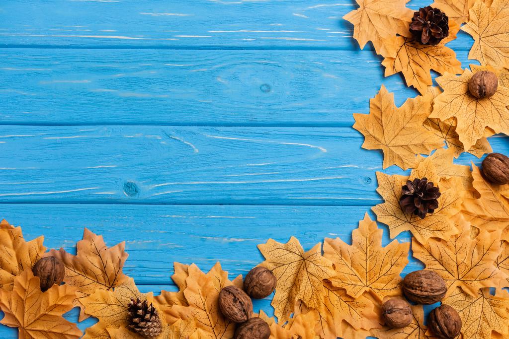 vrchní pohled na podzimní zeleň s ořechy a kužely na modrém dřevěném pozadí - Fotografie, Obrázek