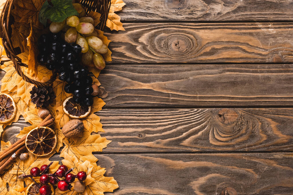 Ansicht der Herbsternte aus Korb auf Laub auf braunem Holzgrund verstreut - Foto, Bild
