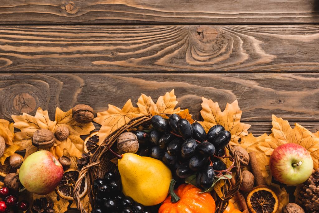 top view of autumnal harvest in basket on foliage on brown wooden background - Photo, Image