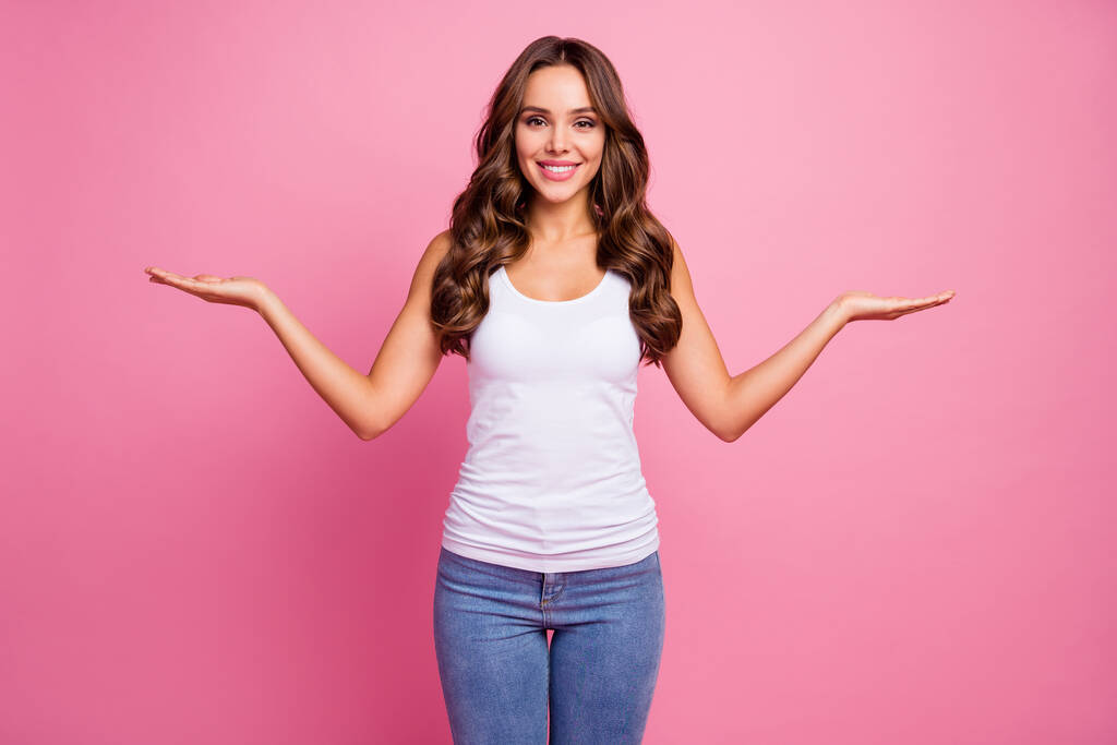 美しい女性のセールスマネージャーの写真は、新しい割引価格の製品を保持していますオープンパーム素敵なオファー最高のバリアントを示す白いカジュアルシングルジーンズ孤立ピンク色の背景を着用 - 写真・画像