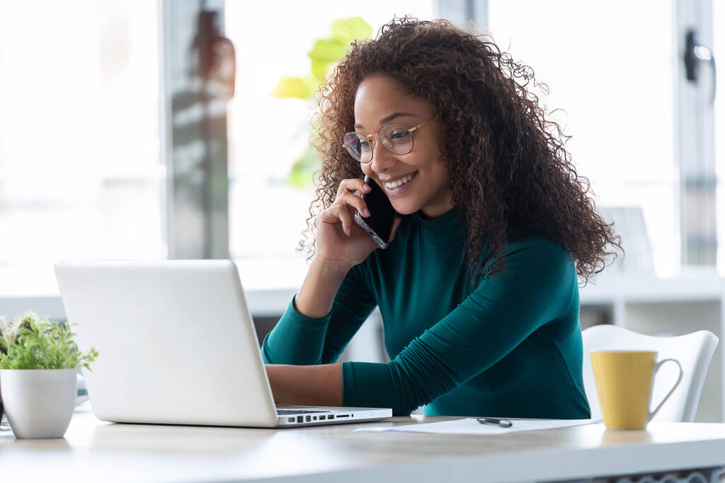 Laukaus kaunis nuori liiketoiminnan nainen puhuu matkapuhelimella työskennellessään hänen kannettava tietokone toimistossa. - Valokuva, kuva