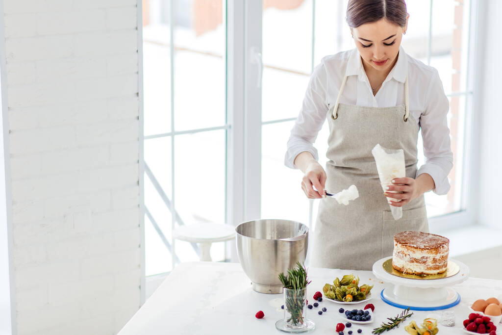 chef donna di talento utilizzando sacchetto di pasticceria durante la cottura - Foto, immagini