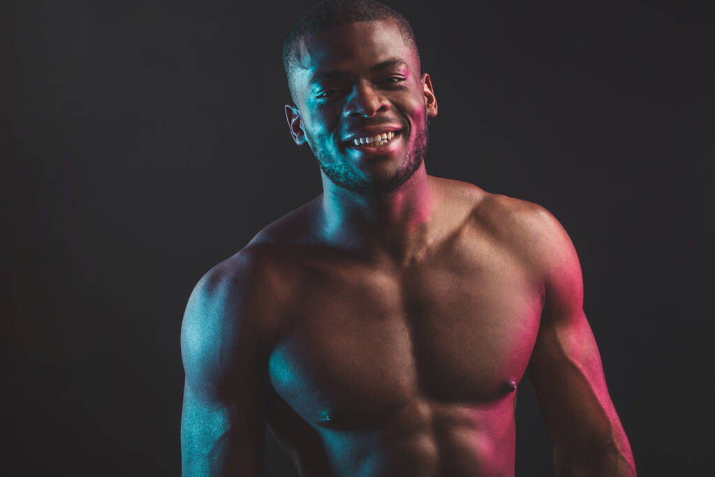 Afrikalı erkek vücut geliştirme şampiyonu çıplak gövdesiyle stüdyoda siyah üzerinde poz veriyor. . - Fotoğraf, Görsel