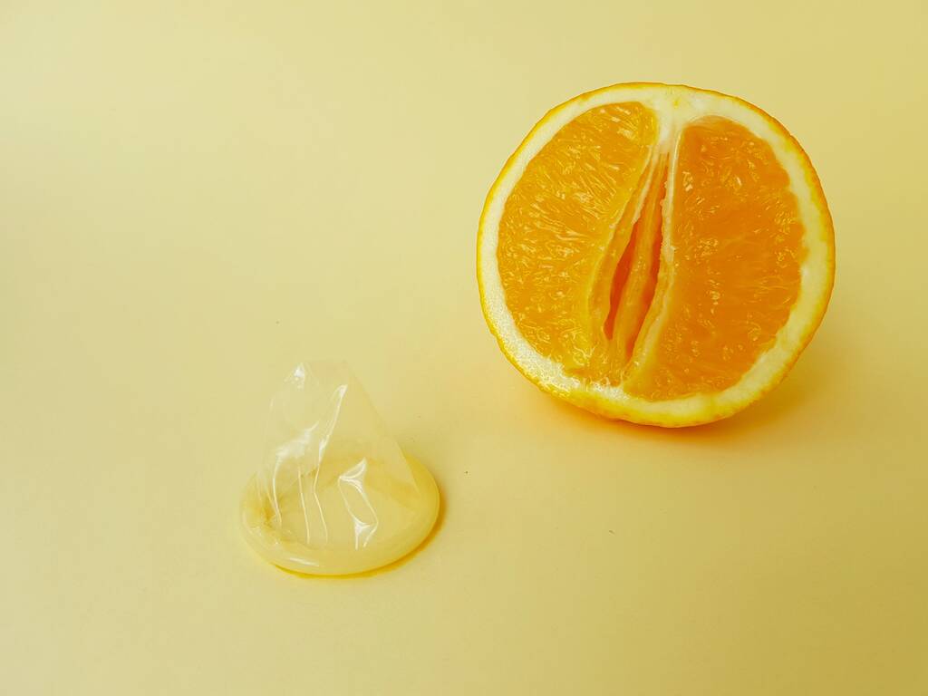 The concept of safe sex and protection. A vagina symbol. A juicy orange and a condom on a bright yellow background. - Fotografie, Obrázek