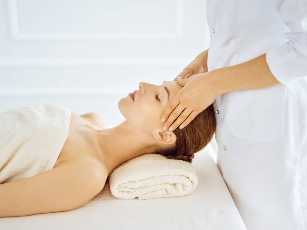 Mulher bonita desfrutando de massagem facial com olhos fechados no centro de spa. Conceito de tratamento relaxante em medicina
 - Foto, Imagem