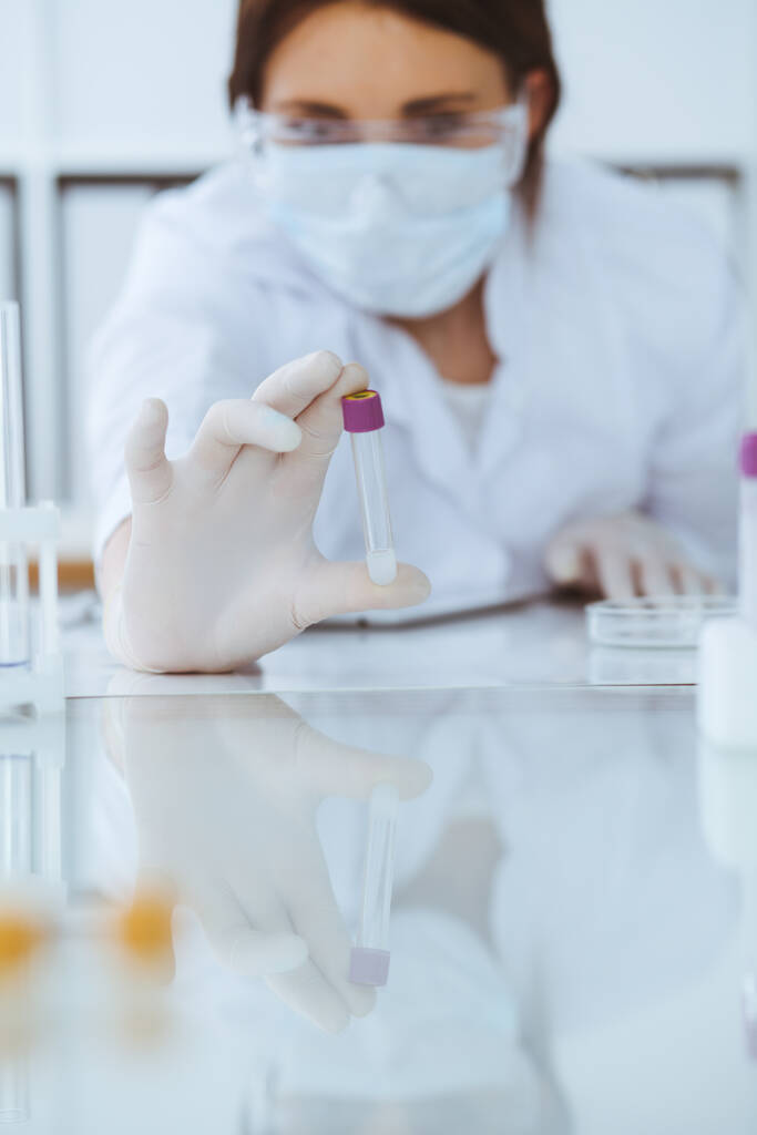 Close-up van professionele vrouwelijke wetenschapper in beschermende brillen die experimenteren met reagentia in het laboratorium. Geneeskunde en onderzoek - Foto, afbeelding