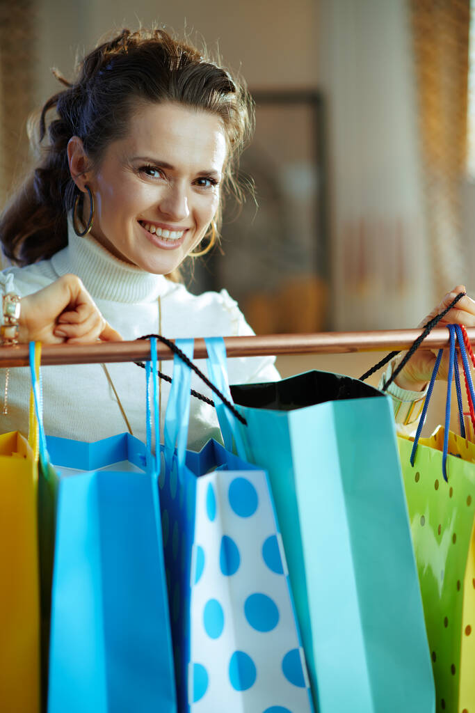 boldog modern középkorú nő fehér pulóver és szoknya keres bevásárló táska lóg réz ruhák sín. - Fotó, kép