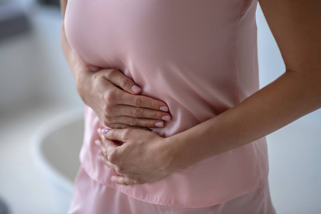 Γυναίκα στα ροζ έχει στομαχόπονο και αγγίζει την κοιλιά της - Φωτογραφία, εικόνα
