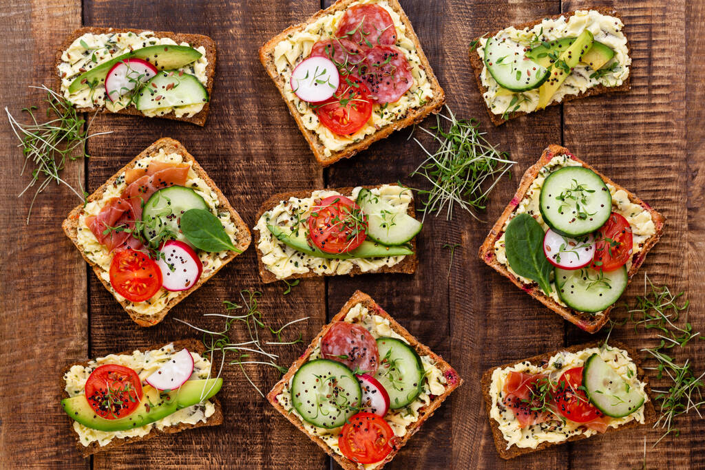 Variety of mini sandwiches with cream cheese, vegetables and salami. Sandwiches with cucumber, radish, tomatoes, salami on a gray background, top view. Flat lay. - Photo, Image