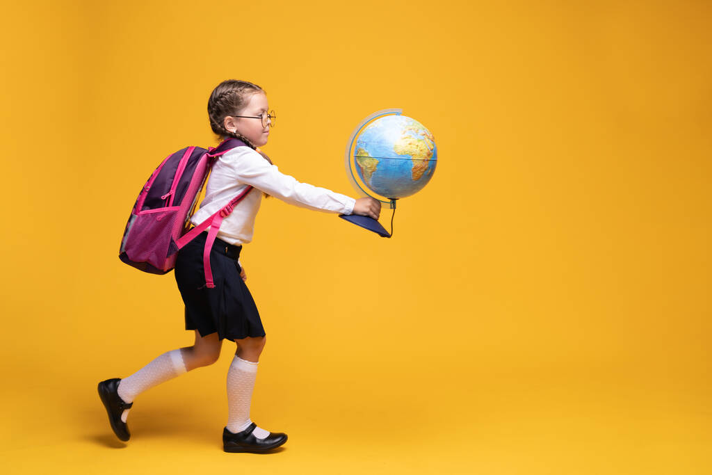 a little girl in school uniform holds a globe in her hands on a yellow background. - Photo, Image