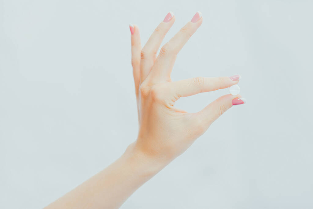 Жіноча рука з французьким манікюром тримає білу круглу таблетку на пальцях. Лікування, медицина, фармакологія
 - Фото, зображення