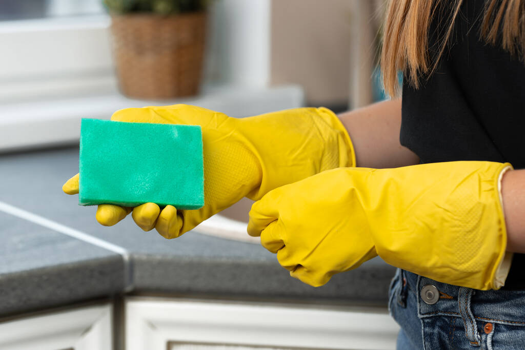 Manos de una mujer con guantes amarillos sosteniendo esponja verde - Foto, Imagen