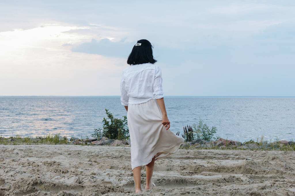 Visão traseira da jovem mulher vestindo camisa branca e saia na praia - Foto, Imagem