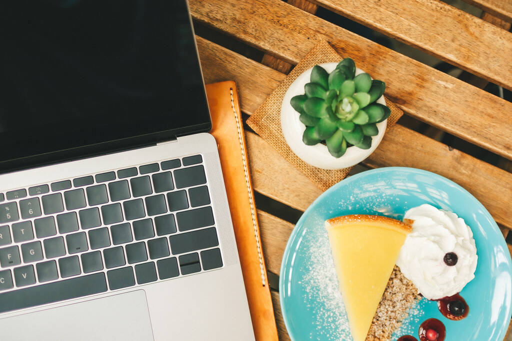 Vue du dessus de l'ordinateur portable sur le bureau avec gâteau au fromage dans Concept de travail heureux. - Photo, image