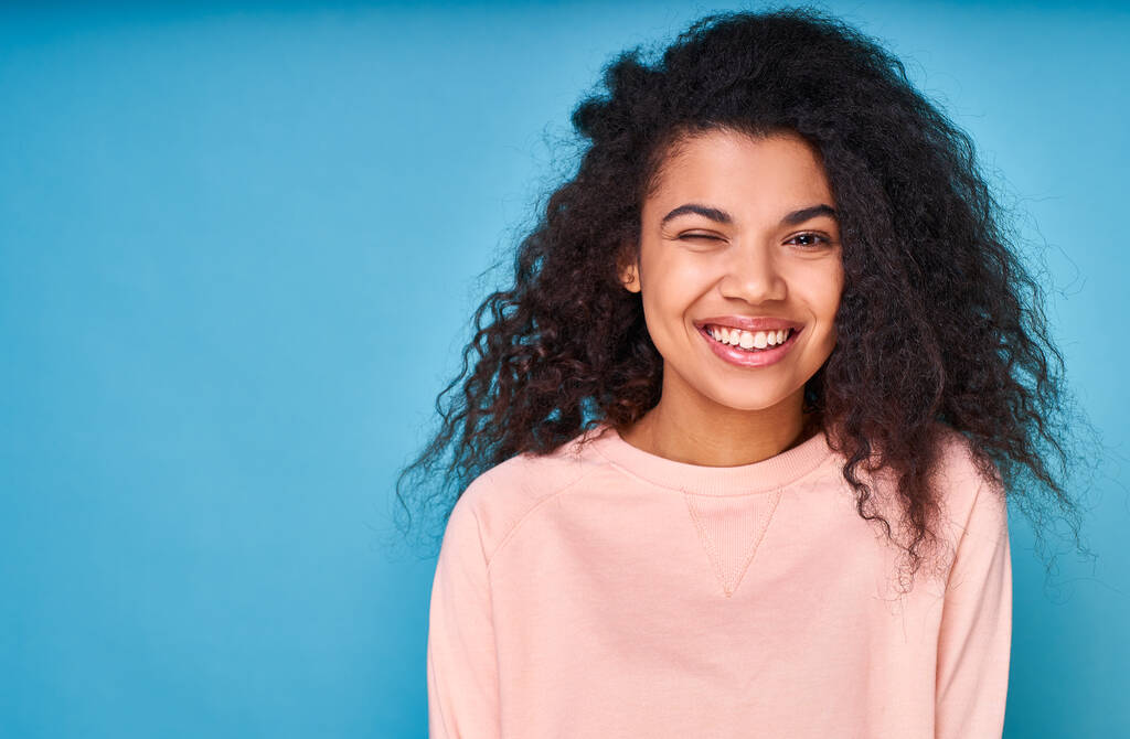 Портрет, позитивний темношкірий кучерявий молода дівчина, відчуває себе енергійним і веселим, носить бежевий светр з довгими рукавами, ізольований на синьому студійному фоні. Копіювати простір
. - Фото, зображення