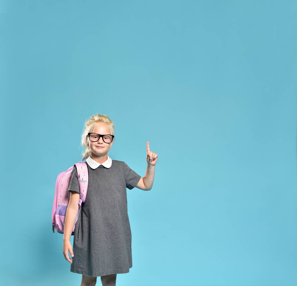 Cute uczennica pokazuje kciuk do wolnego miejsca na niebieskim tle - Zdjęcie, obraz