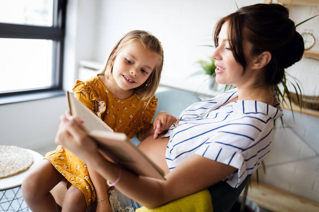 Девочка и ее беременная мать вместе читают книгу. Счастливое семейное время - Фото, изображение