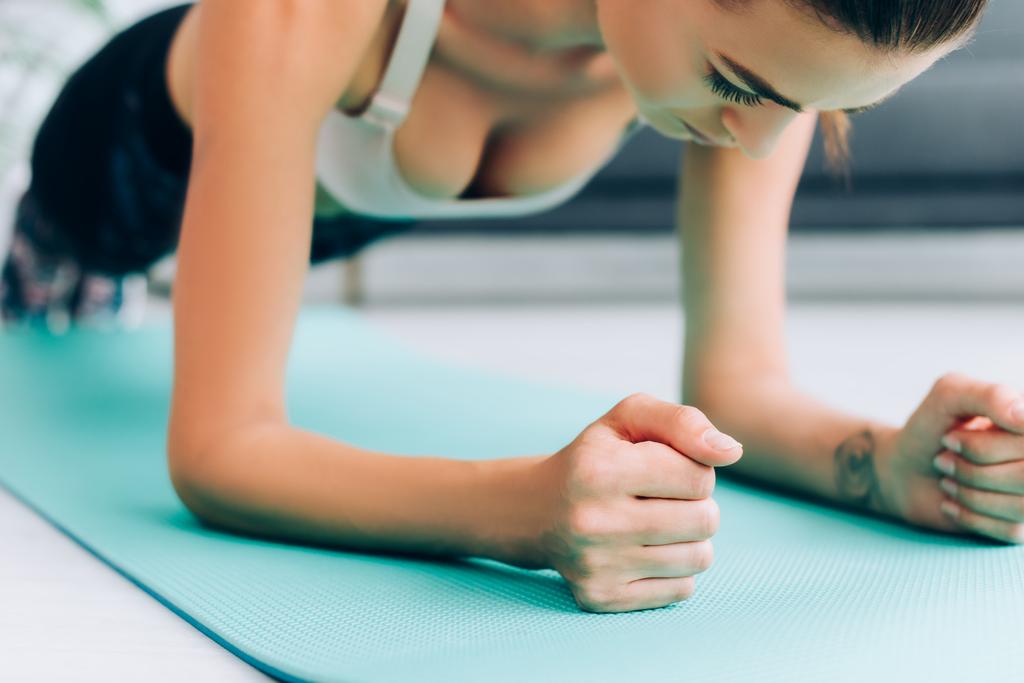 Enfoque selectivo de la deportista haciendo tablón en la alfombra de fitness en casa  - Foto, imagen