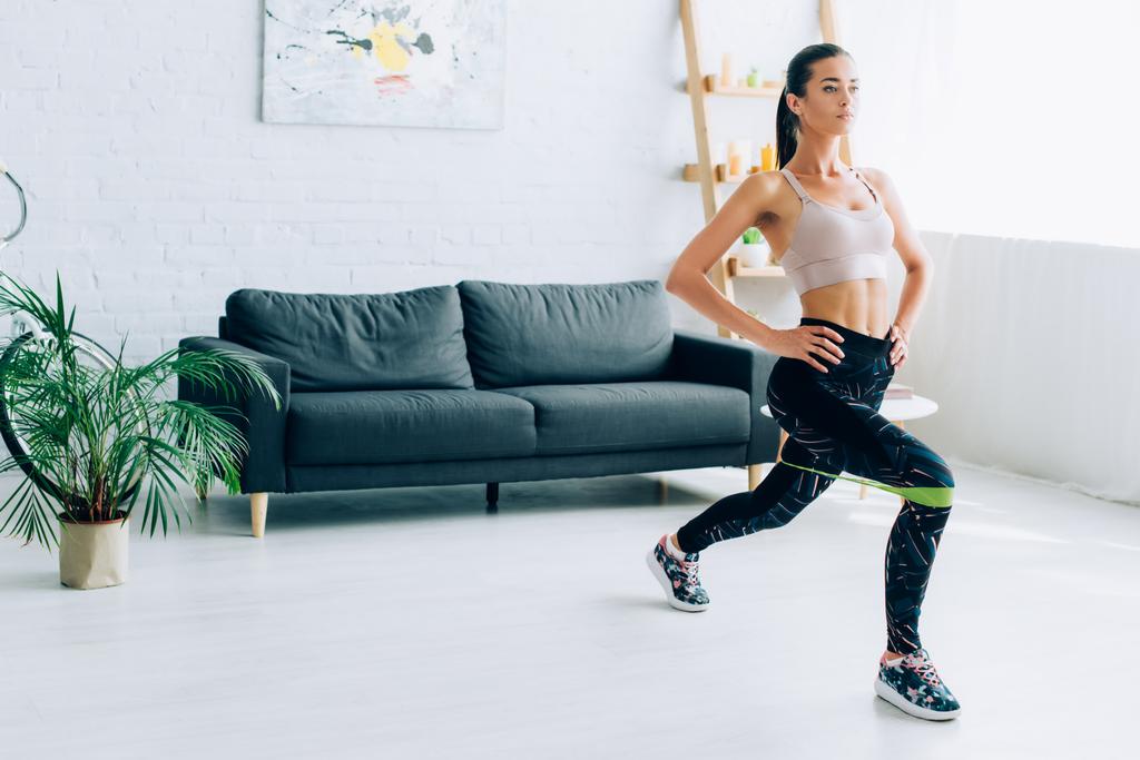 Young sportswoman doing lunges with resistance band at home  - Photo, Image