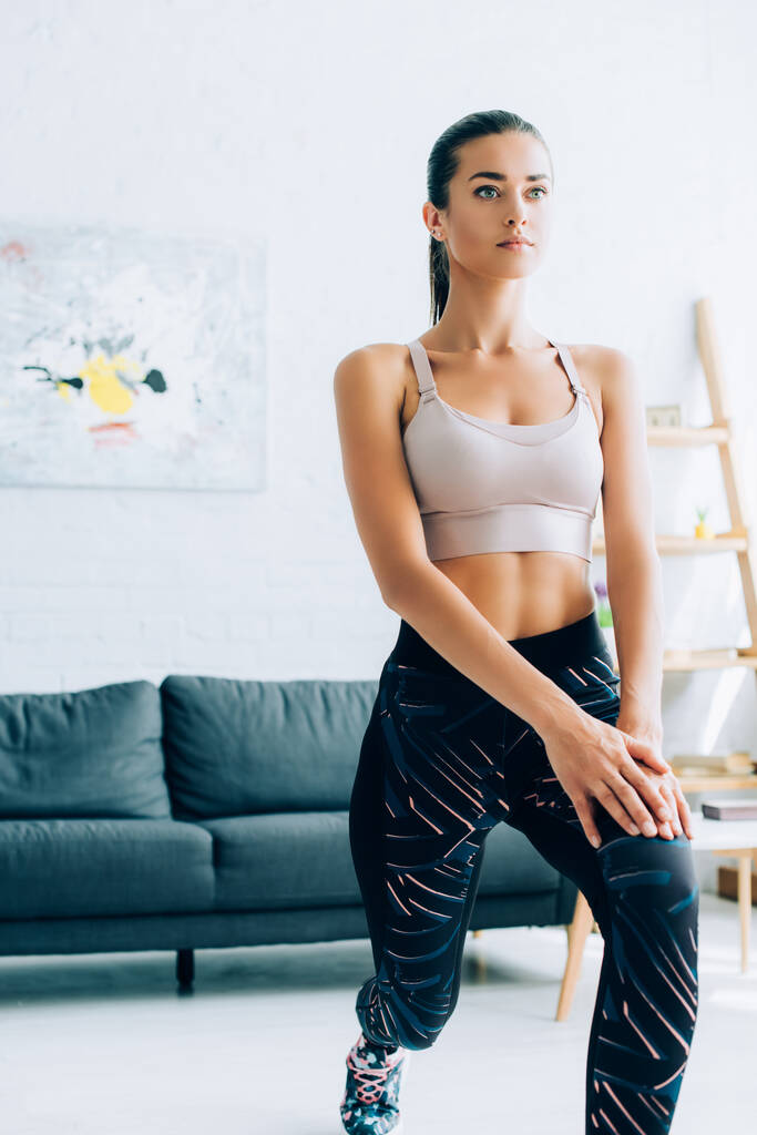 Concentrated woman in sportswear doing lunges in living room  - Photo, Image