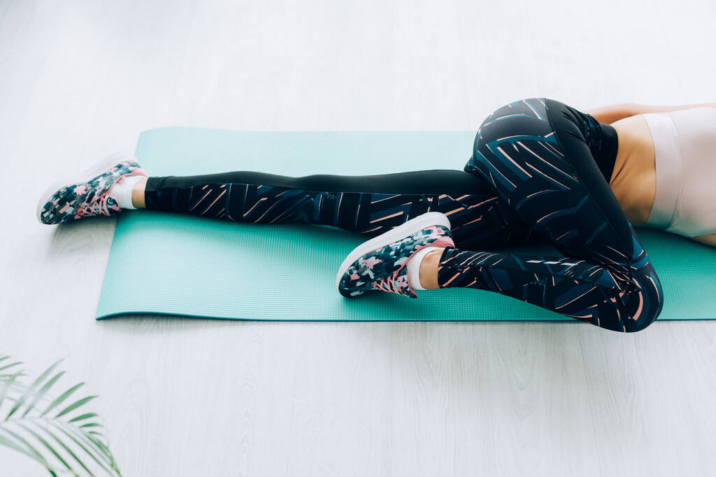 Gebonden zicht op vrouw in sneakers en sportkleding stretching op fitness mat thuis  - Foto, afbeelding