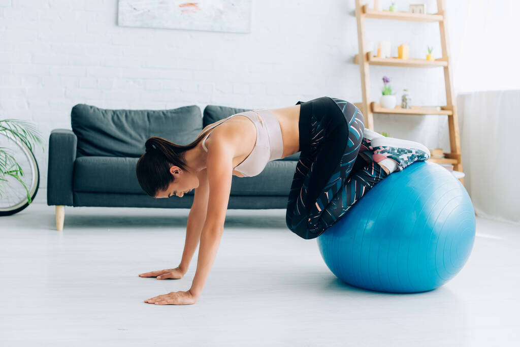 Boční pohled brunetky sportovkyně cvičení s fitness míč v obývacím pokoji  - Fotografie, Obrázek