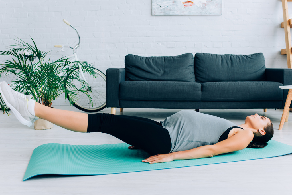 Mujer embarazada haciendo ejercicio en la alfombra de fitness en la sala de estar  - Foto, imagen