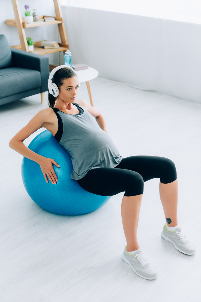 Έγκυος αθλητής σε ακουστικά κατάρτισης με μπάλα γυμναστικής στο σπίτι  - Φωτογραφία, εικόνα
