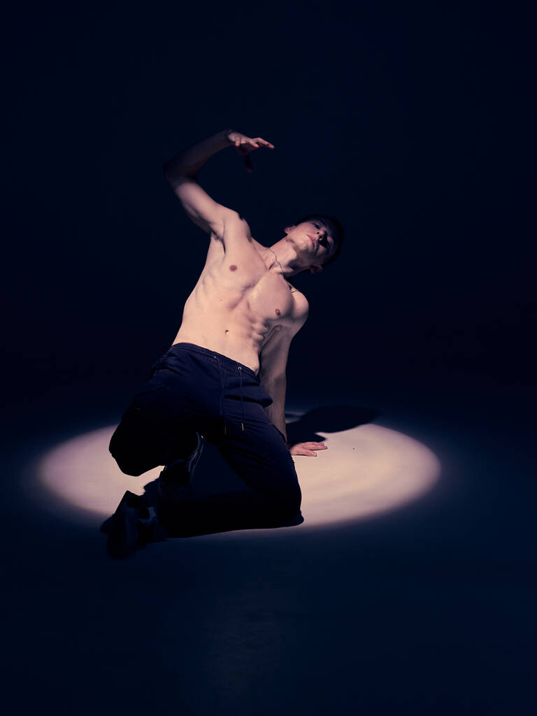 Прохолодний молодий хлопець танцює в студії в центрі уваги на підлозі на чорному тлі
 - Фото, зображення