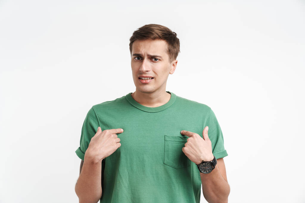 Obraz zdezorientowanego mężczyzny rasy kaukaskiej w podstawowej koszulce proszącego i wskazującego palcem na siebie odizolowanego na białym tle - Zdjęcie, obraz