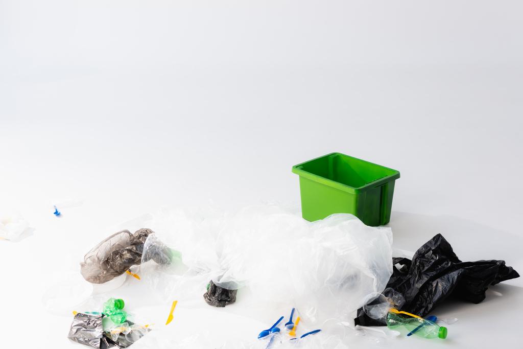 sacchetti di plastica, bottiglie e cucchiai vicino bidone della spazzatura su bianco, concetto di ecologia  - Foto, immagini