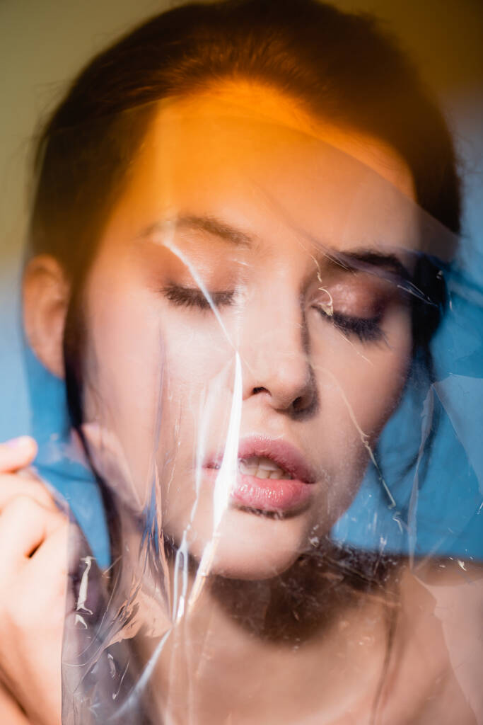 jonge vrouw met gesloten ogen in de buurt van polyethyleen op grijs, ecologie concept  - Foto, afbeelding