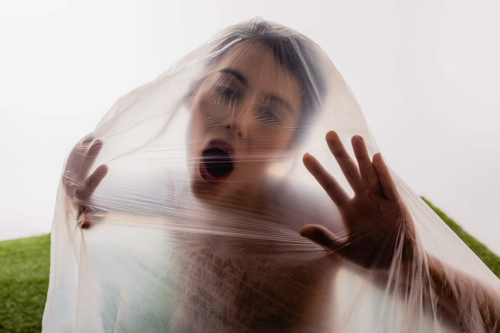 morena mujer gritando a través de polietileno en blanco, concepto de ecología - Foto, imagen