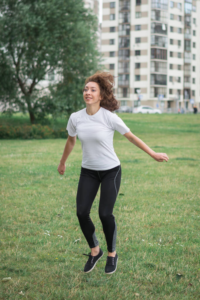 Jonge gespierde fitness vrouw doet squats oefening in het stadspark - Foto, afbeelding