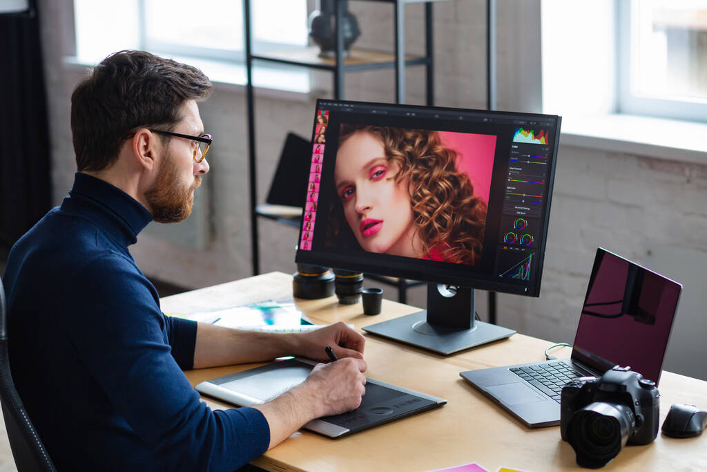 Retouching images in special program.Portrait of graphic designer working in office with laptop,monitor,graphic drawing tablet and color palette.Retoucher workplace in photo studio.Creative agency - Photo, Image