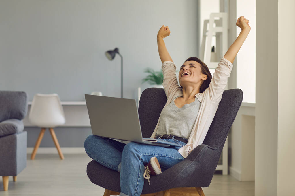 Positive young girl with laptop stretching in cozy armchair after work. Beautiful businesswoman relaxing at home office - Photo, Image