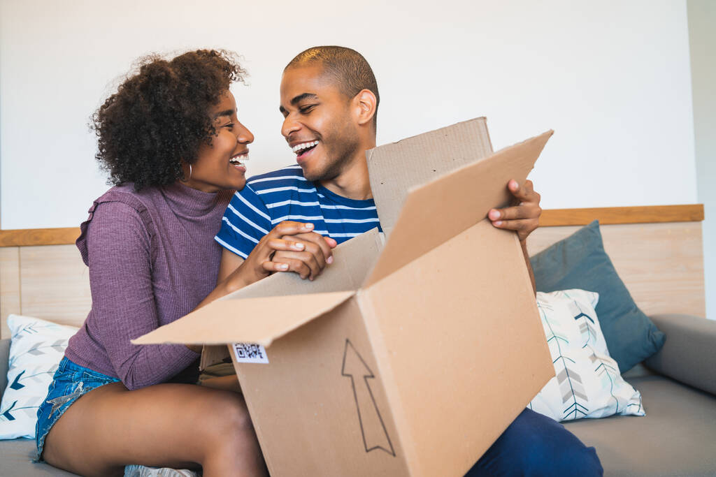 Retrato do jovem casal latino feliz abrindo um pacote em casa. Conceito de entrega, transporte e serviço postal. - Foto, Imagem