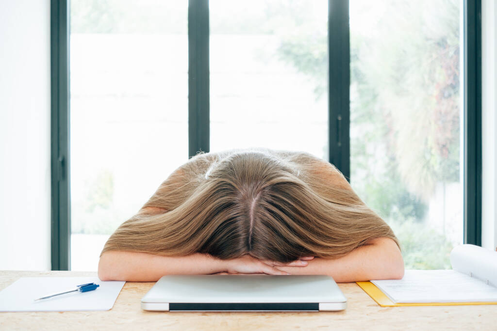 młoda sfrustrowana kobieta położyła głowę na stole pracy, zmęczony pracownik lub student siedzi w domu wyczerpany przed laptopem PC - Zdjęcie, obraz