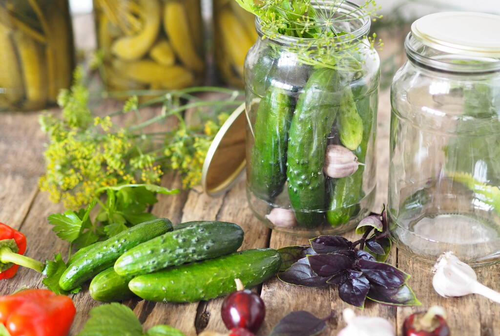 Home remedies for future use. Fresh and pickled cucumbers, homemade canned food with cucumbers in glass jars on a wooden background. - Photo, Image