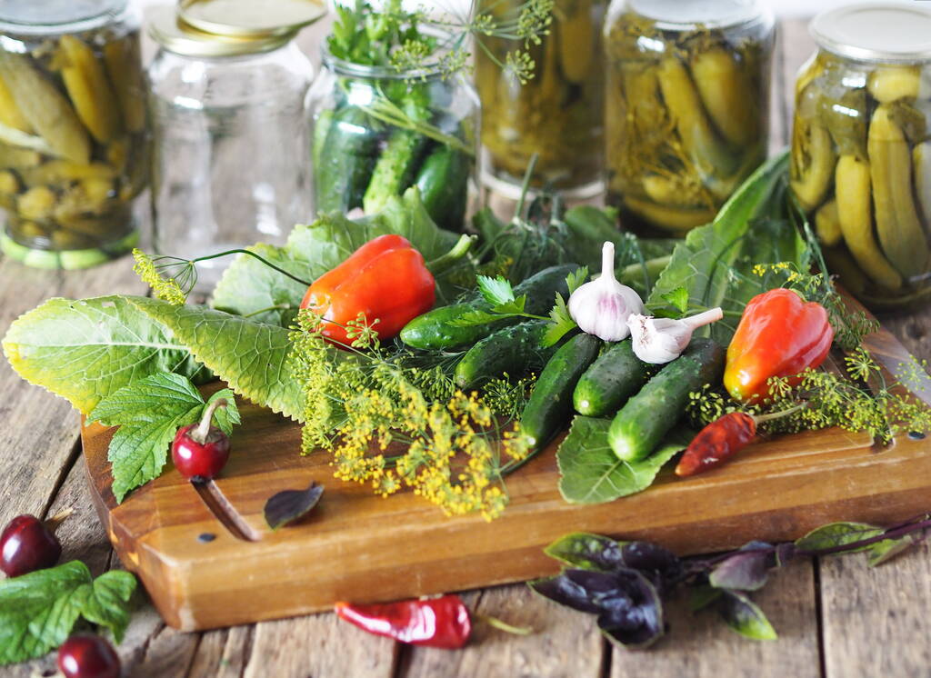 Potten met komkommers, ingrediënten voor het beitsen op een houten oude natuurlijke tafel. Het conserveren van komkommers in glazen potten onder deksels voor opslag in de winter. - Foto, afbeelding