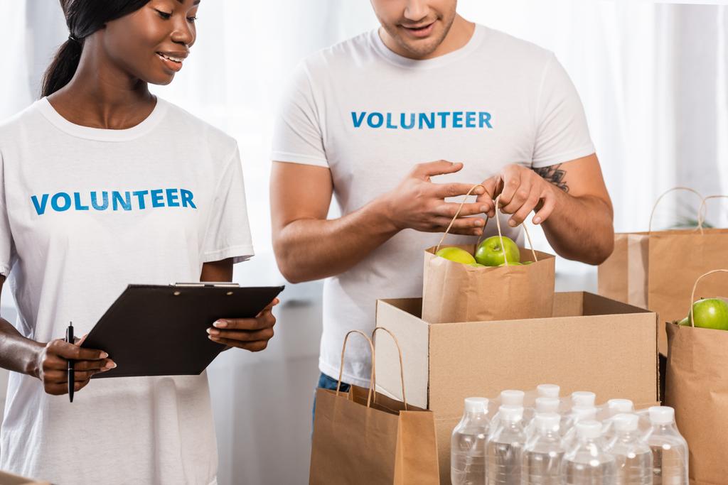 Selektiver Schwerpunkt des Freiwilligenpakets mit Äpfeln in der Nähe einer afrikanisch-amerikanischen Frau mit Klemmbrett  - Foto, Bild