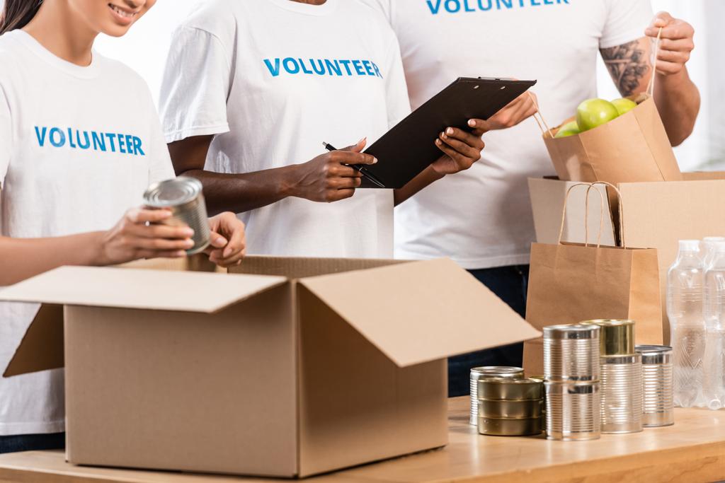 Widok wielokulturowych wolontariuszy z schowkiem pakujących jedzenie na stole w centrum charytatywnym - Zdjęcie, obraz