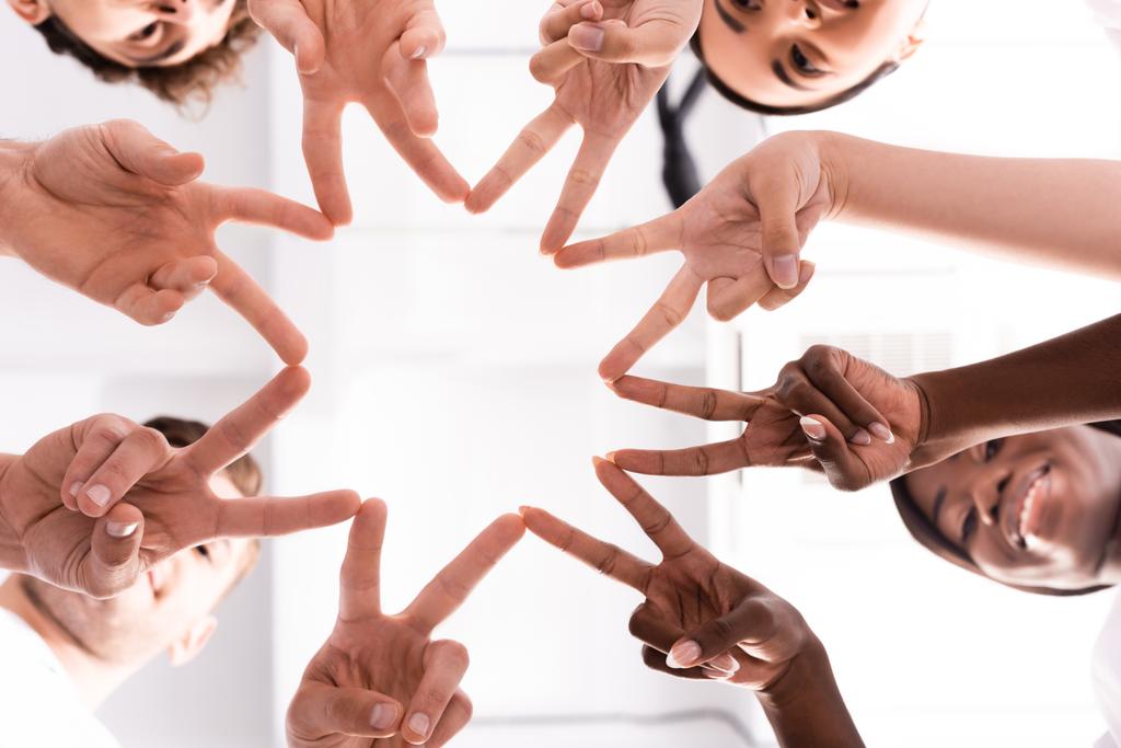 Bottom view of multiethnic volunteers showing peace gesture  - Photo, Image