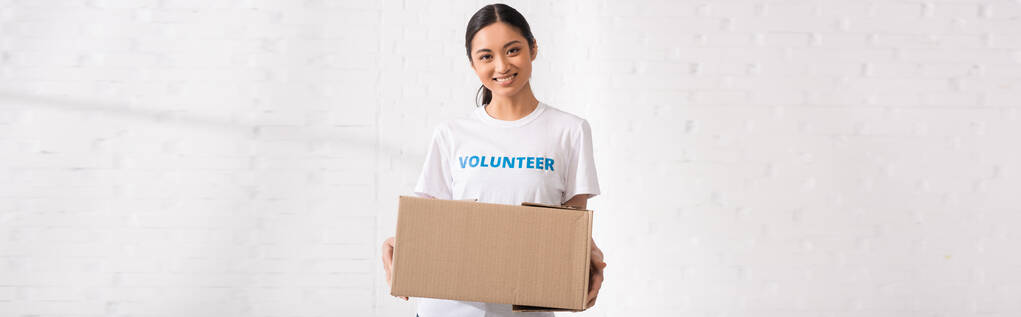 Panoramiczne uprawy azjatyckiej kobiety z literami wolontariuszki na T-shirt gospodarstwa pakiet  - Zdjęcie, obraz