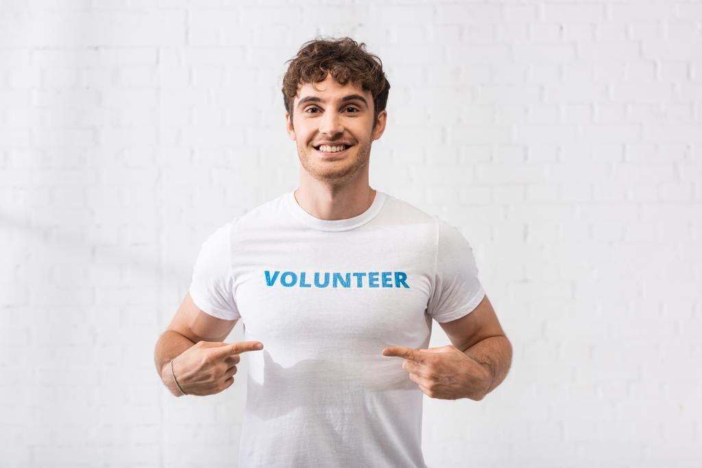 Молодой человек, указывающий пальцами на волонтерскую надпись на футболке  - Фото, изображение