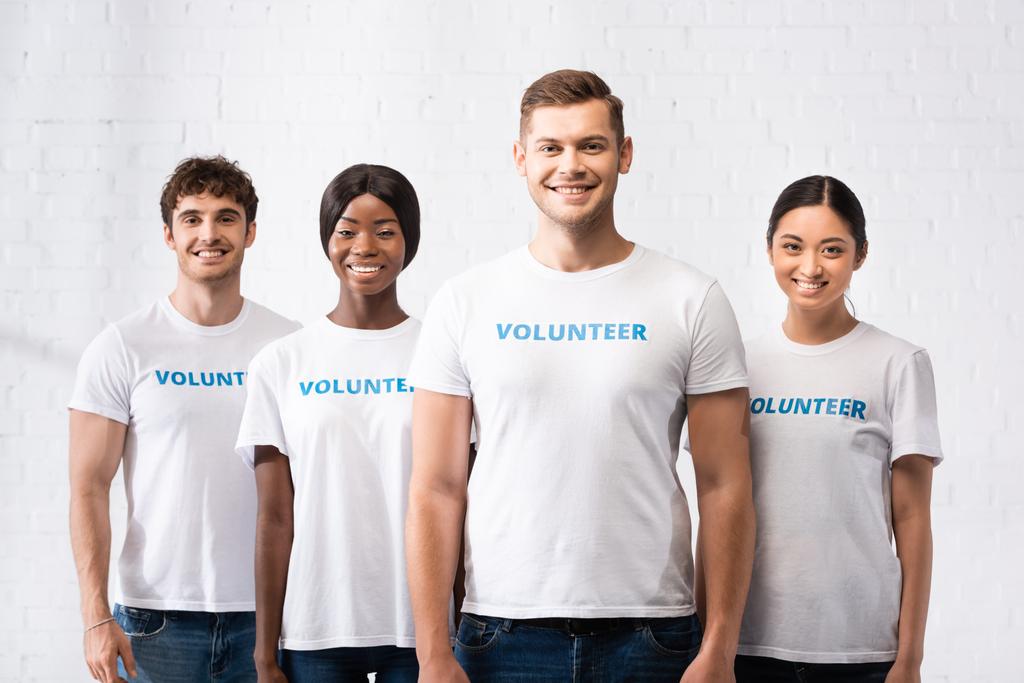Jóvenes voluntarios multiétnicos en camisetas con letras mirando a la cámara en el centro de caridad  - Foto, imagen
